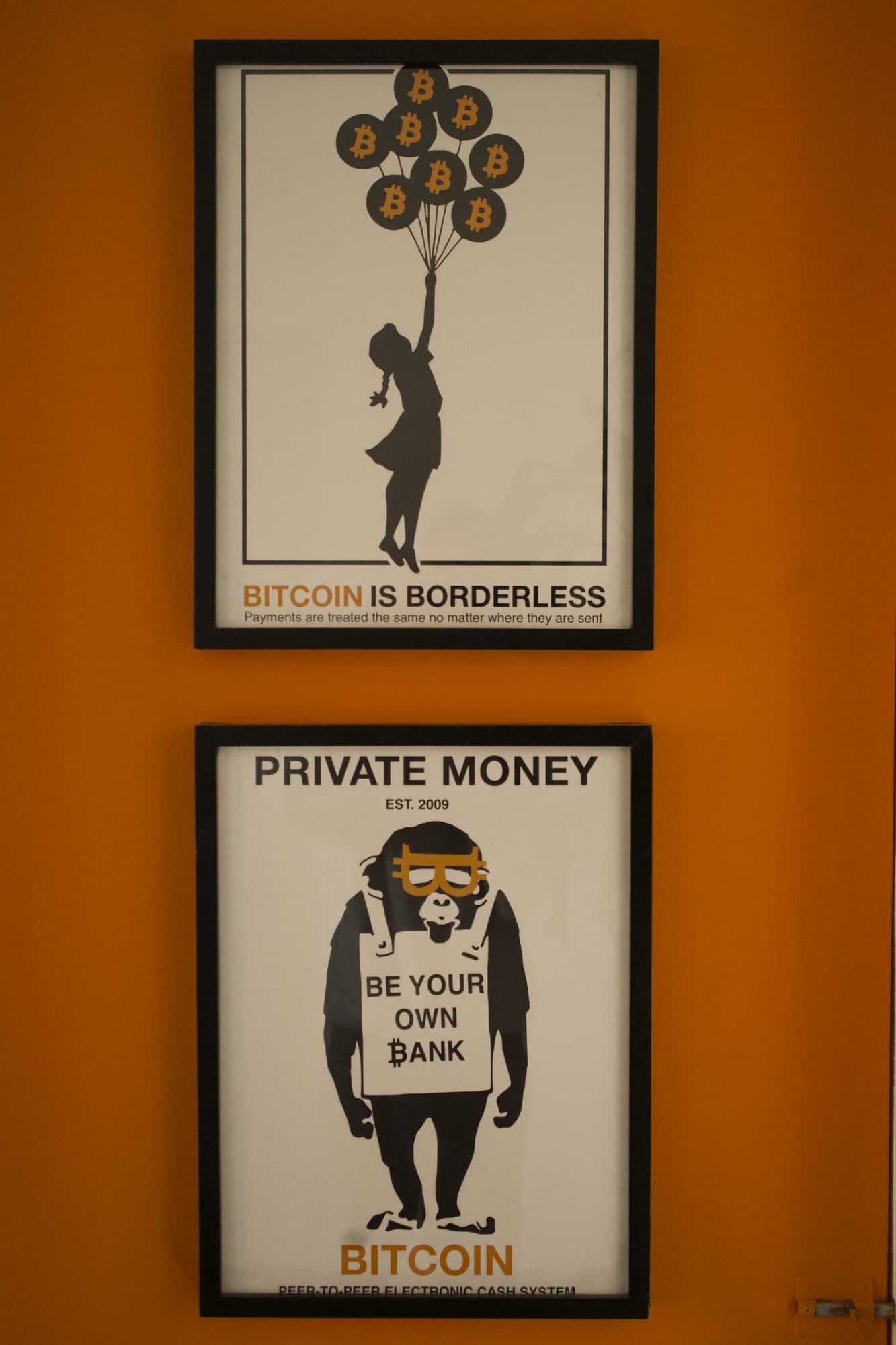 Dos pósters de Bitcoin en una pared naranja: Bitcoin is borderless y Private money